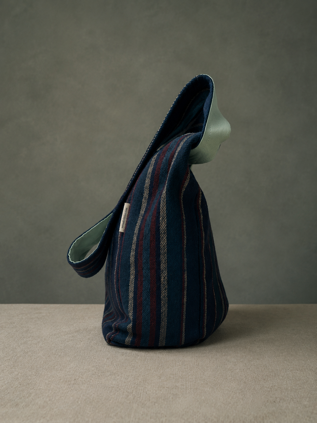 Side view of the Harbor Mint 1/2 Pint Stitch Bag showcasing the navy striped woolen shell, soft structure, adjustable strap, and handcrafted artisan design with mint green lining detail.