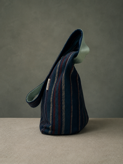 Side view of the Harbor Mint 1/2 Pint Stitch Bag showcasing the navy striped woolen shell, soft structure, adjustable strap, and handcrafted artisan design with mint green lining detail.
