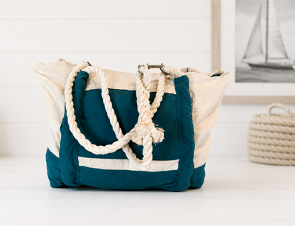 “Front view of a natural canvas tote bag with deep teal contrast trim and matching teal pocket accents, featuring thick white rope handles and a spacious structured design.”