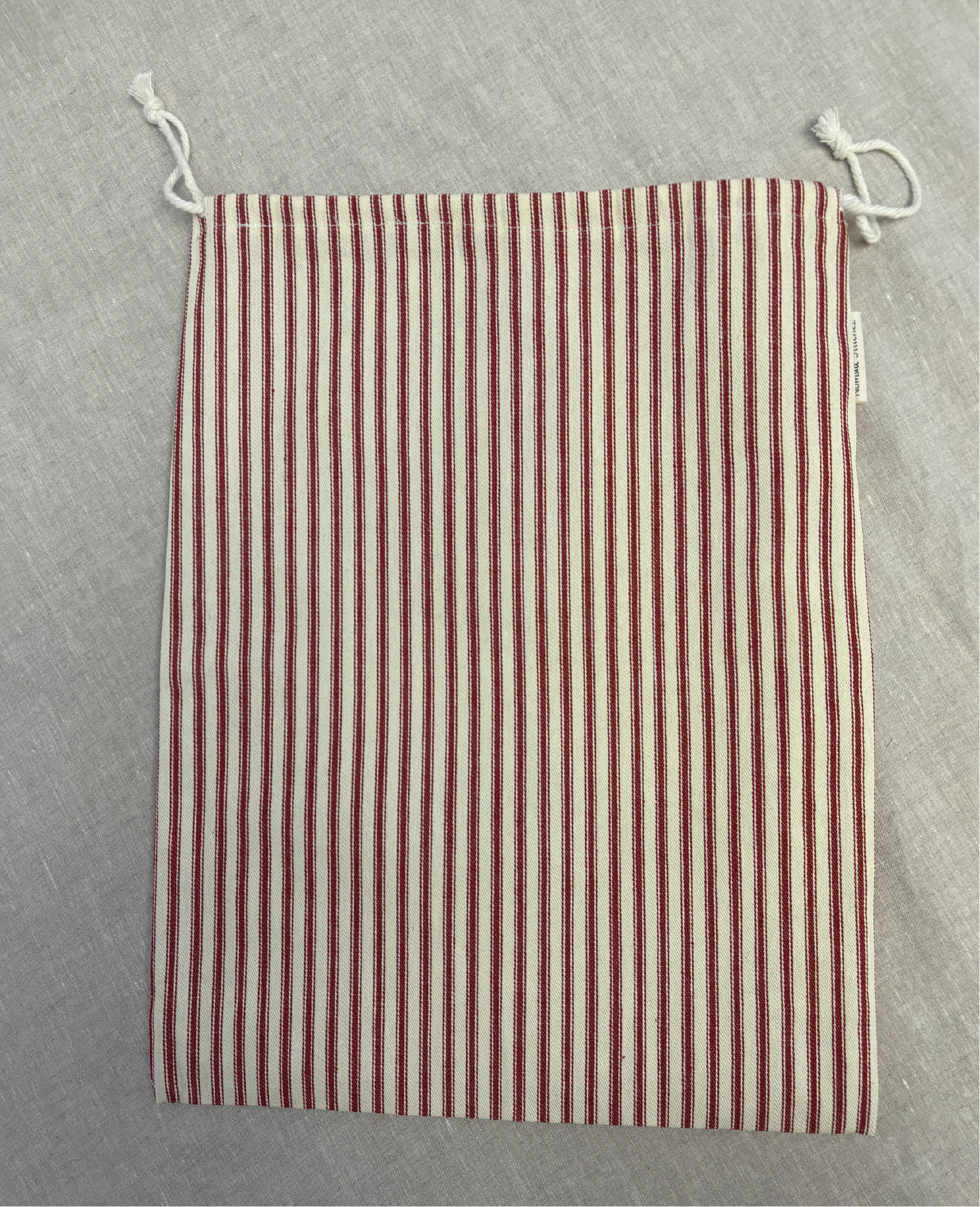 Vertical red stripe cotton utility bag with a cotton drawstring closure, 12in x 15in size, part of the Essentials Collection.