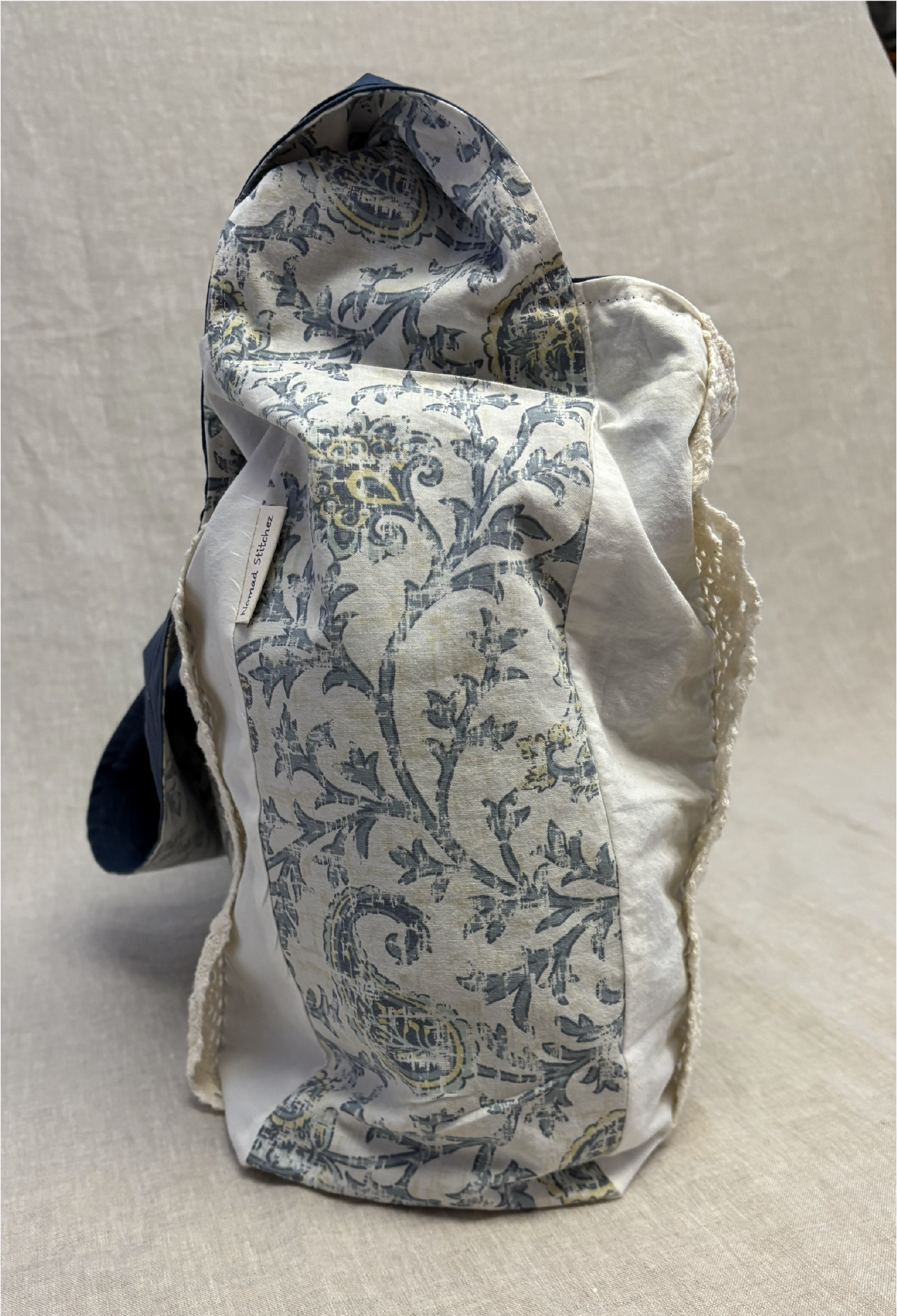 Side view of the blue boho chic floral ½ pint stitch bag showing its slim profile and floral fabric, with the cotton lace accent slightly visible from this angle.
